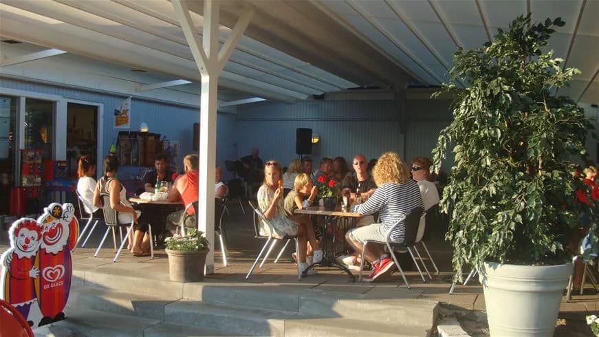 En utomhusmiljö på Klinta Camping med ett bord och stolar placerade på en uteplats. Det finns krukväxter och blommor runtomkring och människor sitter och samtalar i den avkopplande omgivningen.