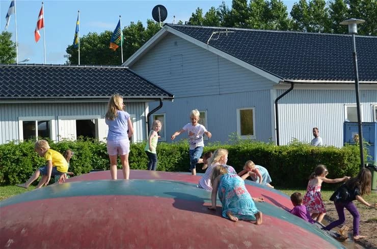 Barn leker på en grön gräsmatta med lekutrustning utomhus, omgivna av en avslappnad och rolig semesterstämning på Klinta camping.