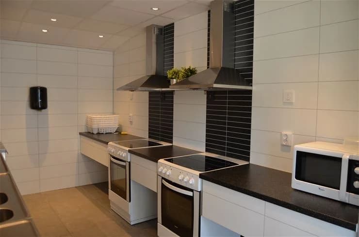 En modern köksmiljö med ett välpolerat golv och ljusa bänkskivor. Kökets tak har inbyggda lampor, och rummet är utrustat med spis och andra vitvaror. En del av Klinta Camping.