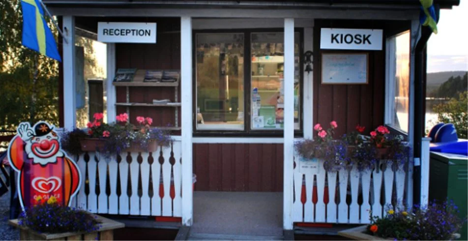 En liten kiosk med en dörr, belägen vid Sölje Camping, omgiven av grönska och utomhusstruktur.