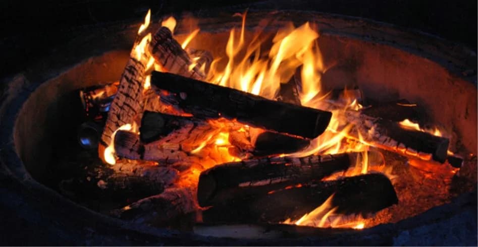 En levande lägereld på Sölje camping, med flammande orange lågor och glödande kol.