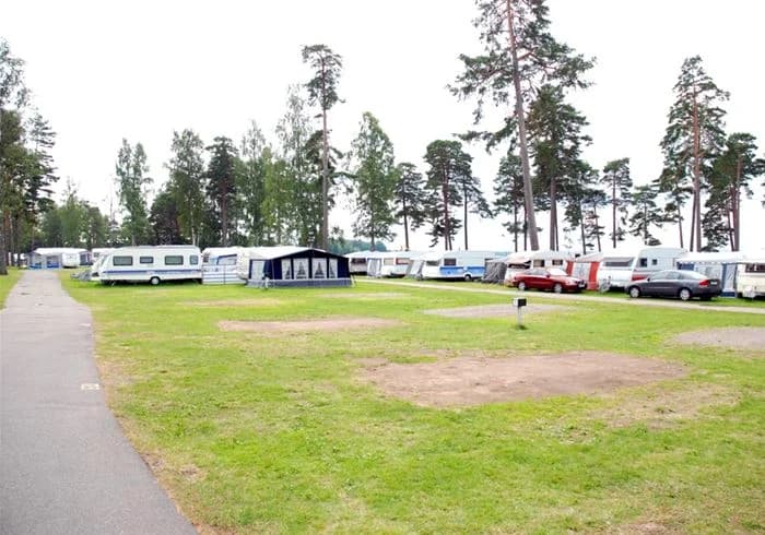En öppen gräsyta med parkerade husbilar på Karlsborgs camping, omgiven av träd och en flaggstång i bakgrunden.