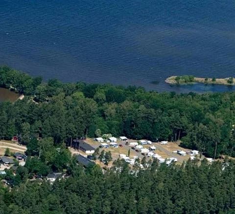 Flygfoto över Bromölla Camping & Vandrarhem, beläget vid en pittoresk kustlinje med vik och strand, omgiven av naturskön miljö och grönska.