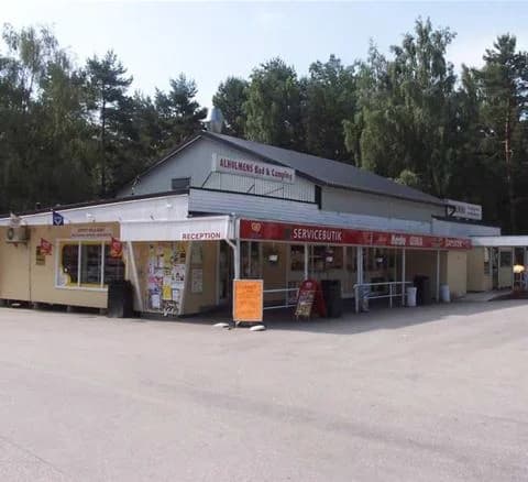 En asfalterad parkering vid Bromölla Camping & Vandrarhem, med en sport-utility vehicle synlig i förgrunden och bakgrundens rastplatsanläggningar.