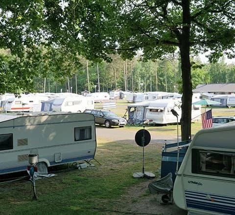 En husvagn parkerad på grusplan vid Bromölla Camping & Vandrarhem, omgiven av grönskande träd i bakgrunden.