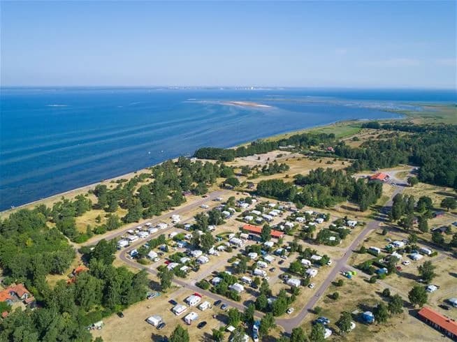 Fågelperspektiv över Haga Park Camping & Stugor med vy över kusten, där sandstranden möter havet och landskapet breder ut sig längs bukten.
