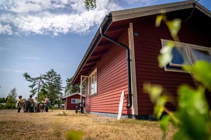 En mysig stuga med träfasad och sadeltak, omgiven av gröna gräsmattor och trädgårdsbyggnader i Haga Park Camping & Stugor.