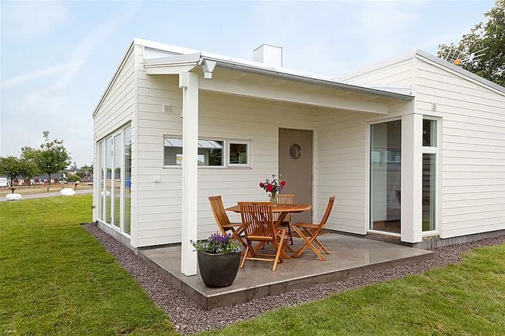 En stuga med träfasad och veranda, omgiven av en välskött trädgård på Köpingbadens camping.