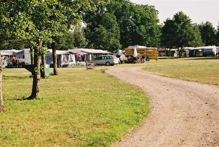 En campingplats med tält och husbilar uppställda bland träd som ger skugga, i en välskött parkmiljö.