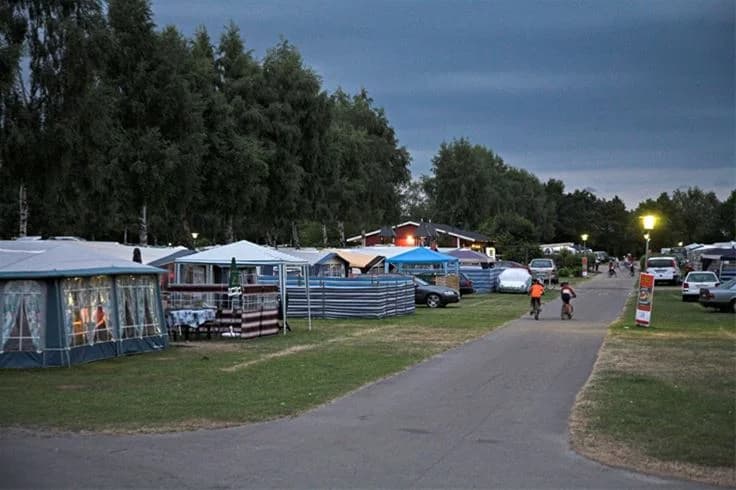 En campingplats i Saxnäs med tält och husbilar uppställda bland träd. Området är öppet för rekreation och besökare njuter av fritidsaktiviteter i naturskön miljö.