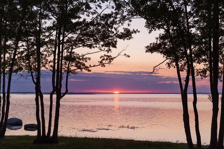 En vacker solnedgång vid Saxnäs Camping, där himlen strålar i varma färger och speglas i det lugna vattnet vid horisonten.