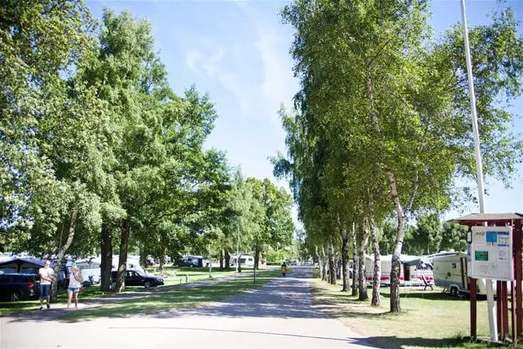 En öppen campingplats i Saxnäs med flera uppställda husbilar, parkerade cyklar och besökare som njuter av utomhusaktiviteter.