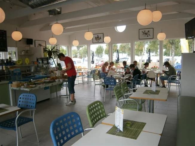 Interiör av en restaurang på Saxnäs camping med möblerade bord och stolar, taklampor och glasdetaljer.