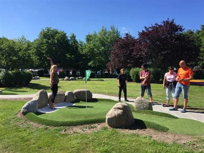 En grönskande campingplats omgiven av gräs och växter, med människor som njuter av friluftsliv och avkoppling.