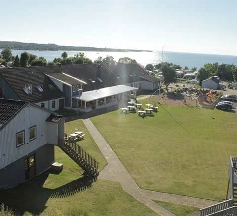 En campingplats med grönskande gräsmattor och omgivande skog, synliga stugor och öppna ytor för besökare att njuta av naturen.