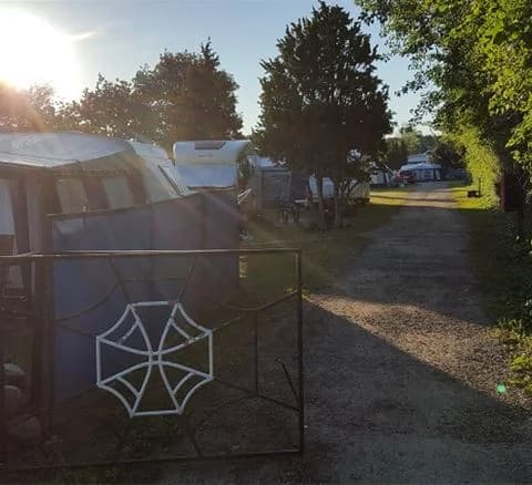 En campingplats med parkerade bilar och husbilar, tält i bakgrunden, och en grön gräsyta vid Klinta Camping.