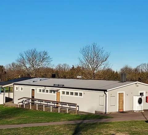 En grönskande campingområde på Klinta Camping med en välskött gräsmatta, små trädgårdsbyggnader och en vedbod.