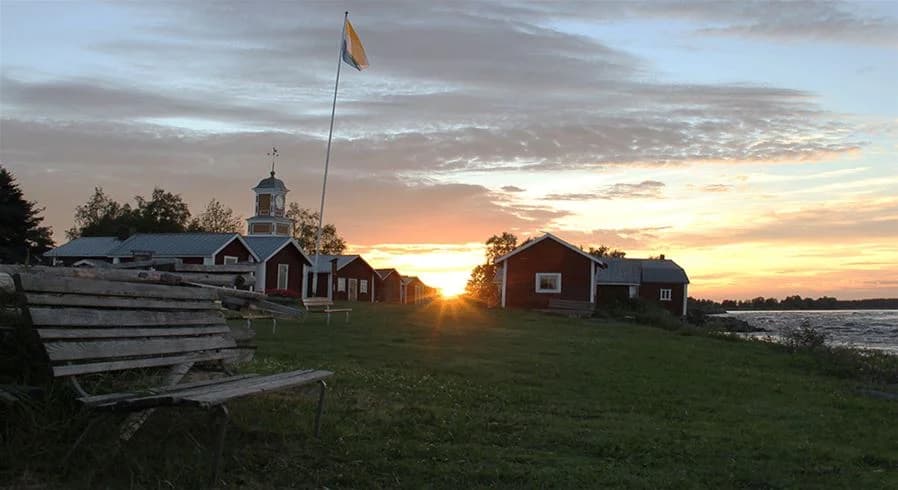 En vacker solnedgång över Kukkolaforsen, himlen färgad i mjuka toner av rött och orange, speglande i det strömmande vattnet.