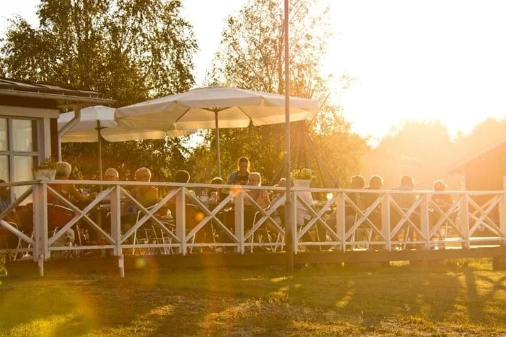 Bild av en utomhusrestaurang vid Kukkolaforsen, med bord och stolar under skuggande parasoller. Champagneglas står på borden, och ett tält finns i bakgrunden.
