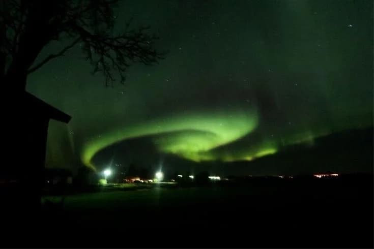 Nattbild av Kukkolaforsen med ett spektakulärt norrsken som sveper över den stjärnklara himlen.
