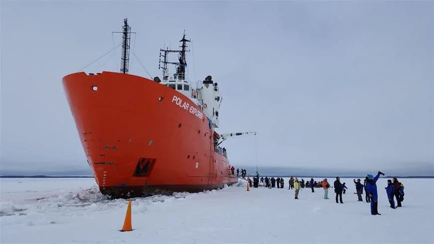 Alt-text: En vintrig scen vid Kukkolaforsen med snötäckt mark och frusna vattendrag. I förgrunden syns en båt täckt av snö samt isformationer runt omkring.