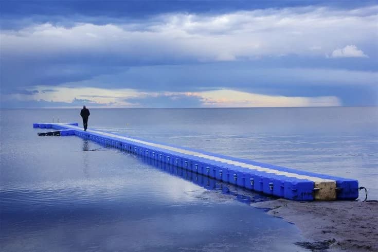 En träbrygga som sträcker sig ut i det blå havet med horisonten i bakgrunden, under en klarblå himmel.