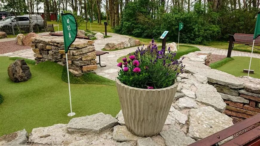 Alt-text: En välskött minigolfbana omgiven av grön konstgräsmatta och anlagda trädgårdsytor vid Stenåsa Stugor & Camping.
