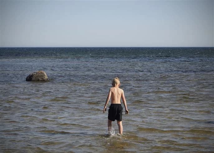 En somrig strandbild vid Stenåsa stugor & camping som visar vågorna slå mot stranden och glada besökare som njuter av solen och vattnets svalka.