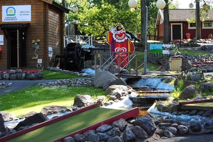 En bild av Eksjö Camping & Konferens som visar en del av deras rekreationsområde med en minigolfbana omgiven av grönska.
