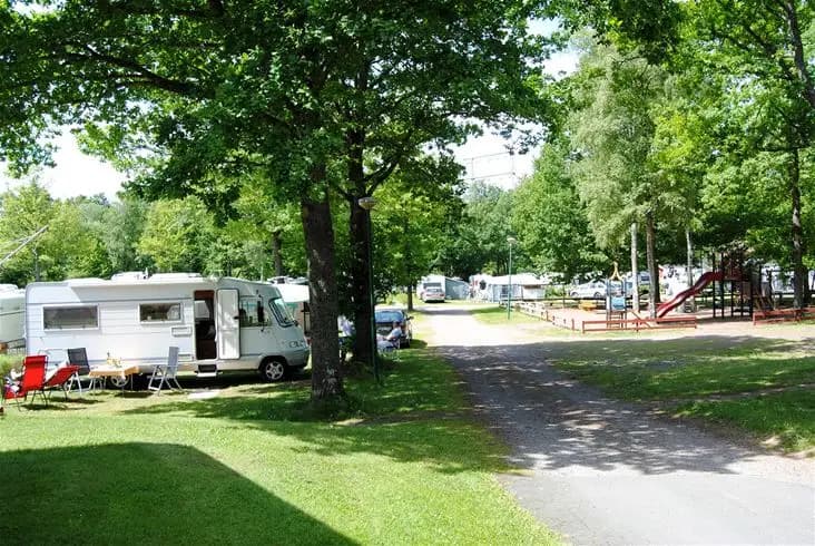 Ett campingområde i Eksjö med gröna träd och vältrimmade gräsmattor. Husvagnar är parkerade på platsen under skuggande träd.