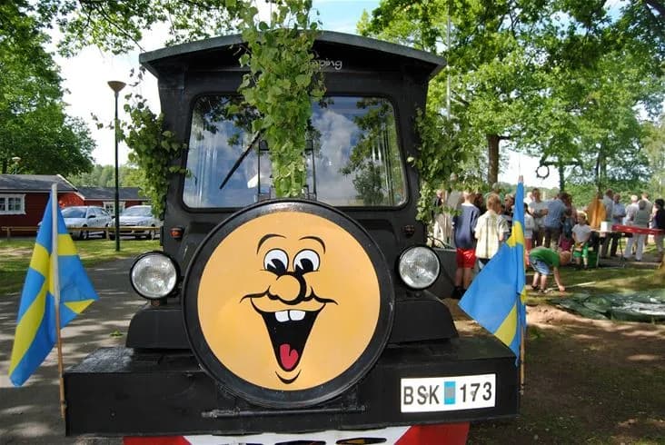En bro över en lugn sjö omgiven av grönska vid Eksjö Camping & Konferens, med en solnedgång i bakgrunden som reflekteras i vattnet. Transportmöjligheter inkluderar cyklar och kanoter, vilket framhäver de natursköna upplevelserna på platsen.