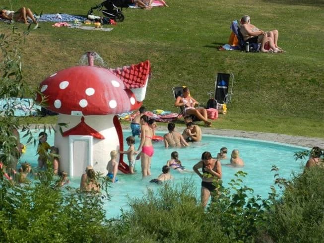 En grupp människor njuter av en solig dag vid Sannabadet, där de kopplar av och har roligt på stranden i sina badkläder. Sommarmiljön skapar en känsla av semester och avkoppling.