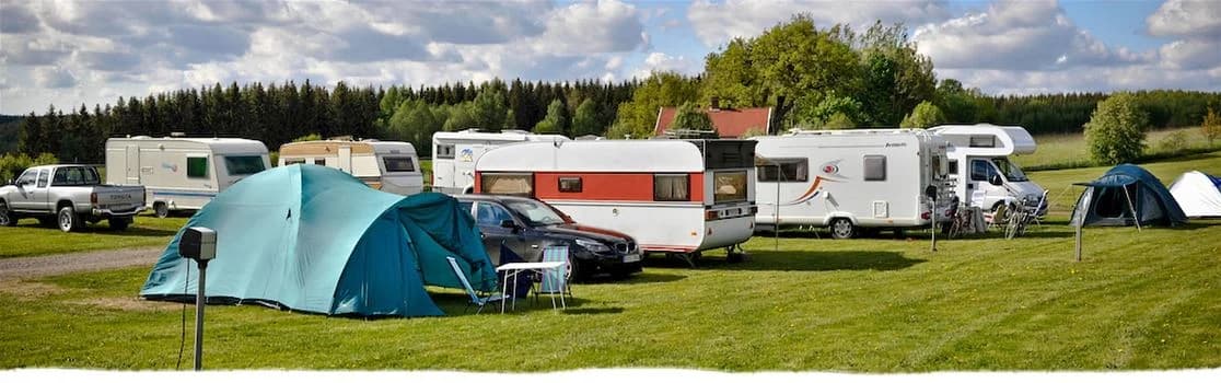 En campingplats vid Sannabadet med husvagnar, tält och husbilar uppställda i en grön parkmiljö.