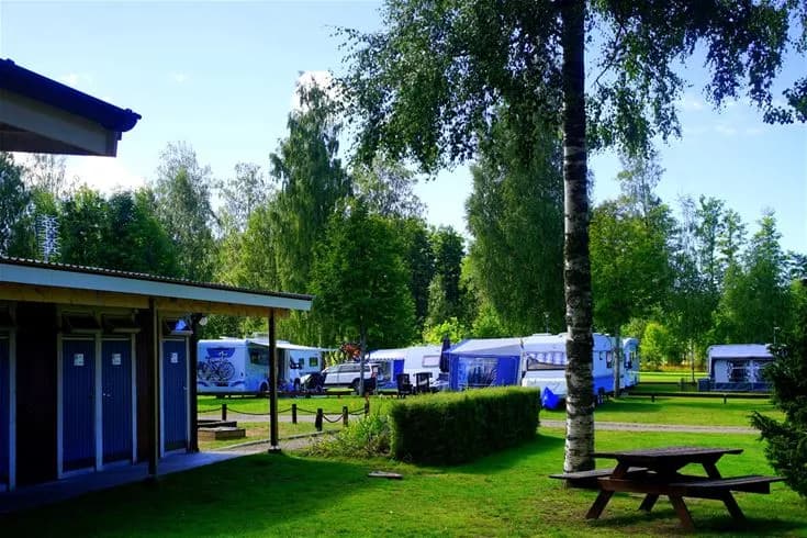 En grönskande campingplats med träd och gräsytor, skuggiga delar och en välskött parkmiljö vid Otterbergets bad och camping.
