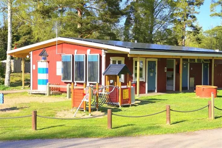 En somrig campingplats med grönskande gräsmattor, skuggiga träd och små stugor, perfekt för rekreation och avkoppling.