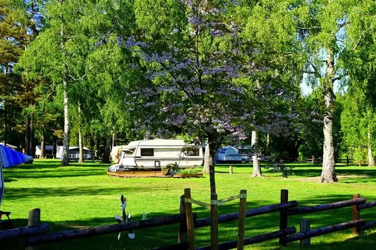 En grönskande campingplats vid Otterbergets bad med träd och gräsmattor, husvagnar och skuggiga områden.