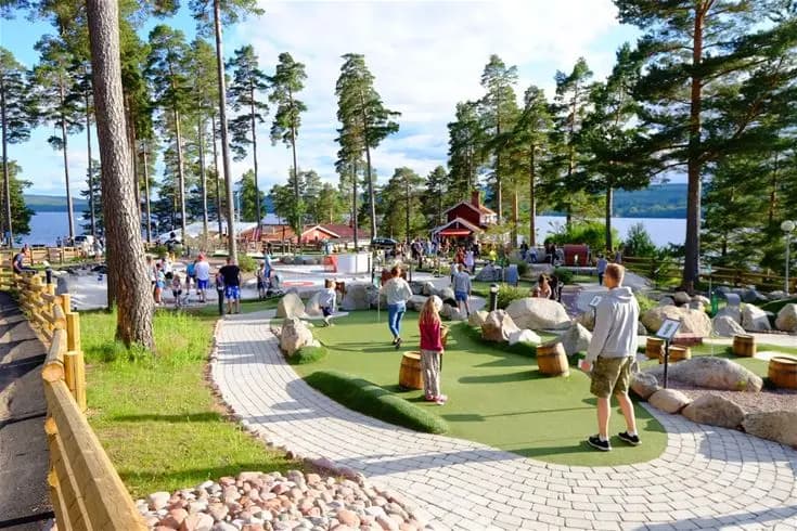 En utomhusmiljö på Leksand Resort med trädgårdslandskap, solstolar och picknickbord, omgiven av grönska och en avslappnande atmosfär perfekt för rekreation och semester.