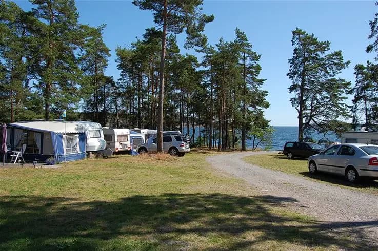 En husbil står parkerad nära en kustlinje vid Tättö havsbad & camping, med en strand och bukt i bakgrunden.