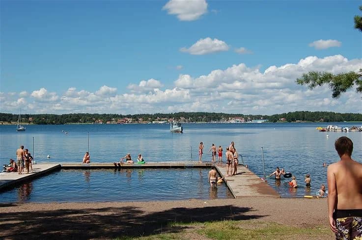 En grupp människor njuter av soligt väder och badar vid en sandstrand vid havet, omgiven av klart vatten. Passar för sommarsemester och avkoppling vid kust och strand.