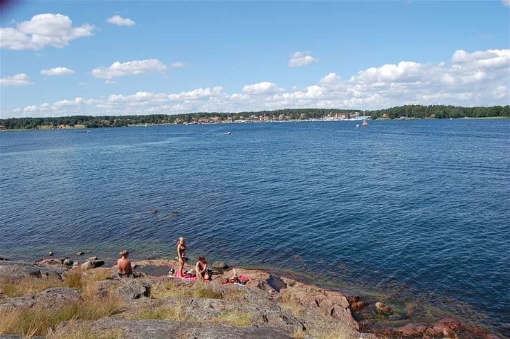 En somrig vy över kustlandskapet vid tättö havsbad & camping, med ett glittrande hav som sträcker ut sig mot horisonten, omgiven av naturliga stränder och rekreationsområden.