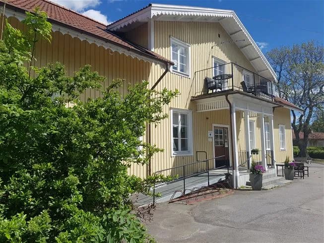 En bild av ett mysigt tättö havsbad & campingområde med flera röda stugor med vita knutar. De omgivande stugorna har traditionellt designade sadeltak, verandor och stora fönster, vilket ger området en inbjudande och hemtrevlig atmosfär.