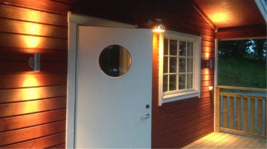 "En mysig trästuga med ljus träpanel och en enkel utomhuslampa, omgiven av grönskande natur på Eksjö Camping & Konferens."