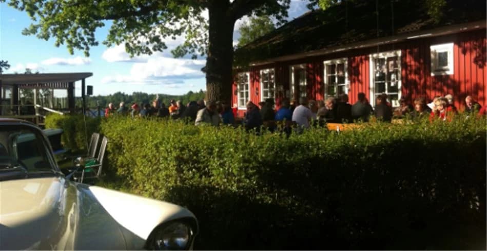 Bild på Eksjö Camping & Konferens: utomhusmiljö med utemöbler, bestående av stolar och bord, inbjudande för gäster att sitta och njuta. I bakgrunden syns en restaurang eller liknande anläggning för servering. Stämningen är avkopplande och välkomnande.