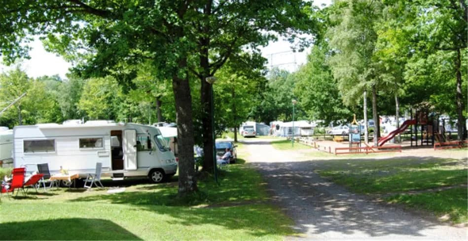Bild av Eksjö Camping & Konferens, visar en naturskön campingplats med träd och husvagnar parkerade i närheten. En lugn parkmiljö som erbjuder rekreation och övernattning bland naturen.