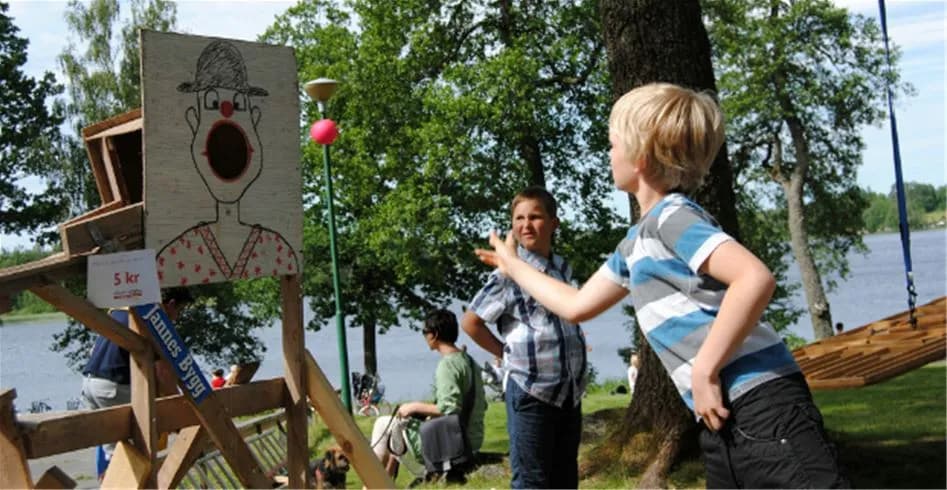 En somrig scen på Eksjö Camping & Konferens där barn leker och har roligt i en parkmiljö, omgiven av grönska och avkopplande atmosfär.