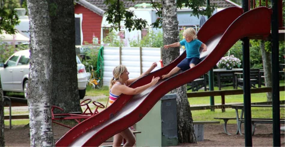 En lekplats med en rutschkana och andra lekredskap omgiven av grönska, där barn leker och har roligt i en offentlig miljö. Perfekt för avkoppling och familjeaktiviteter på Eksjö Camping & Konferens.