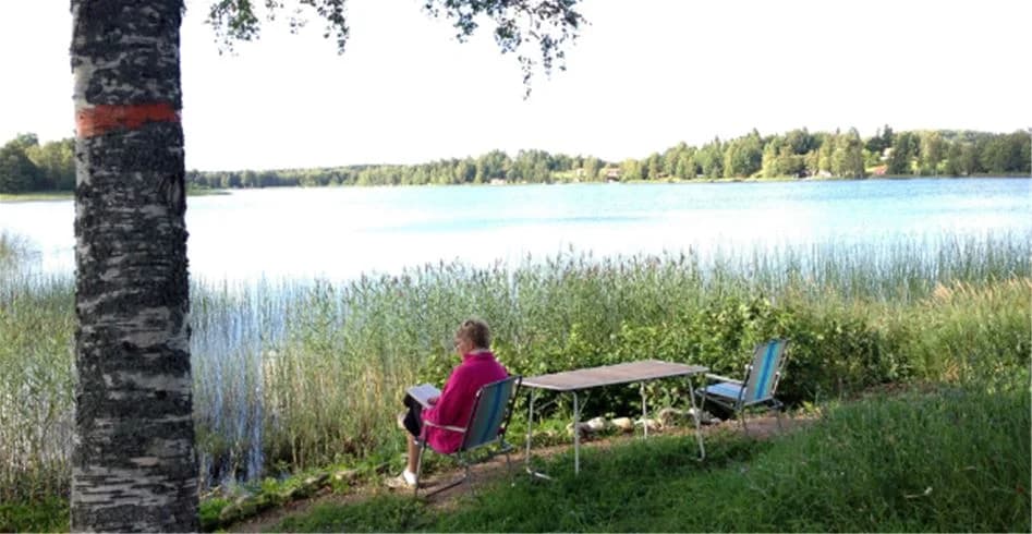Utomhusbild av Eksjö Camping & Konferens med grönt gräs och växter. Det är sommar och utomhusmöbler är placerade på en gräsmatta nära en sjö, vilket skapar en avkopplande atmosfär för besökare.