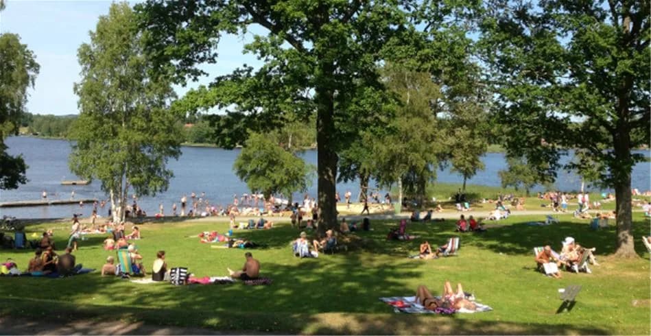En somrig bild av en vattennära plats vid Eksjö Camping & Konferens, med människor som njuter av fritidsaktiviteter vid sjön.