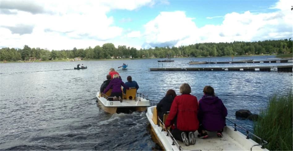 En båt ligger vid sjöstranden på Eksjö Camping & Konferens, omgiven av lugnt vatten och grönskande natur, vilket inbjuder till rekreation och friluftsliv.