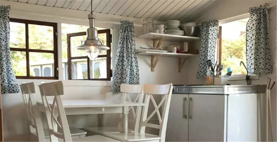 Interiör av en modern campingstuga på Fjällbacka Camping, med möbler och köksinredning i ljust trä, samt ett rymligt rum med ljusa väggar, tak och golv.